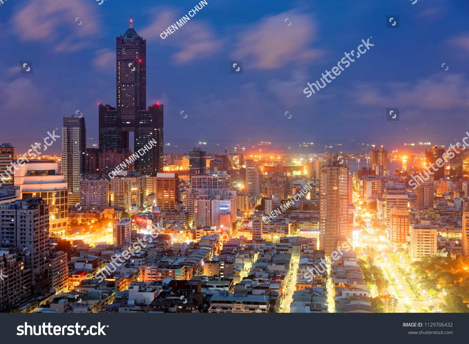 Nightscape of Kaohsiung City, a vibrant seaport in South Taiwan, with the landmark 85 Sky Tower standing among modern buildings, street lights dazzling in blue twilight and ships parking in the harbor #1129706432
