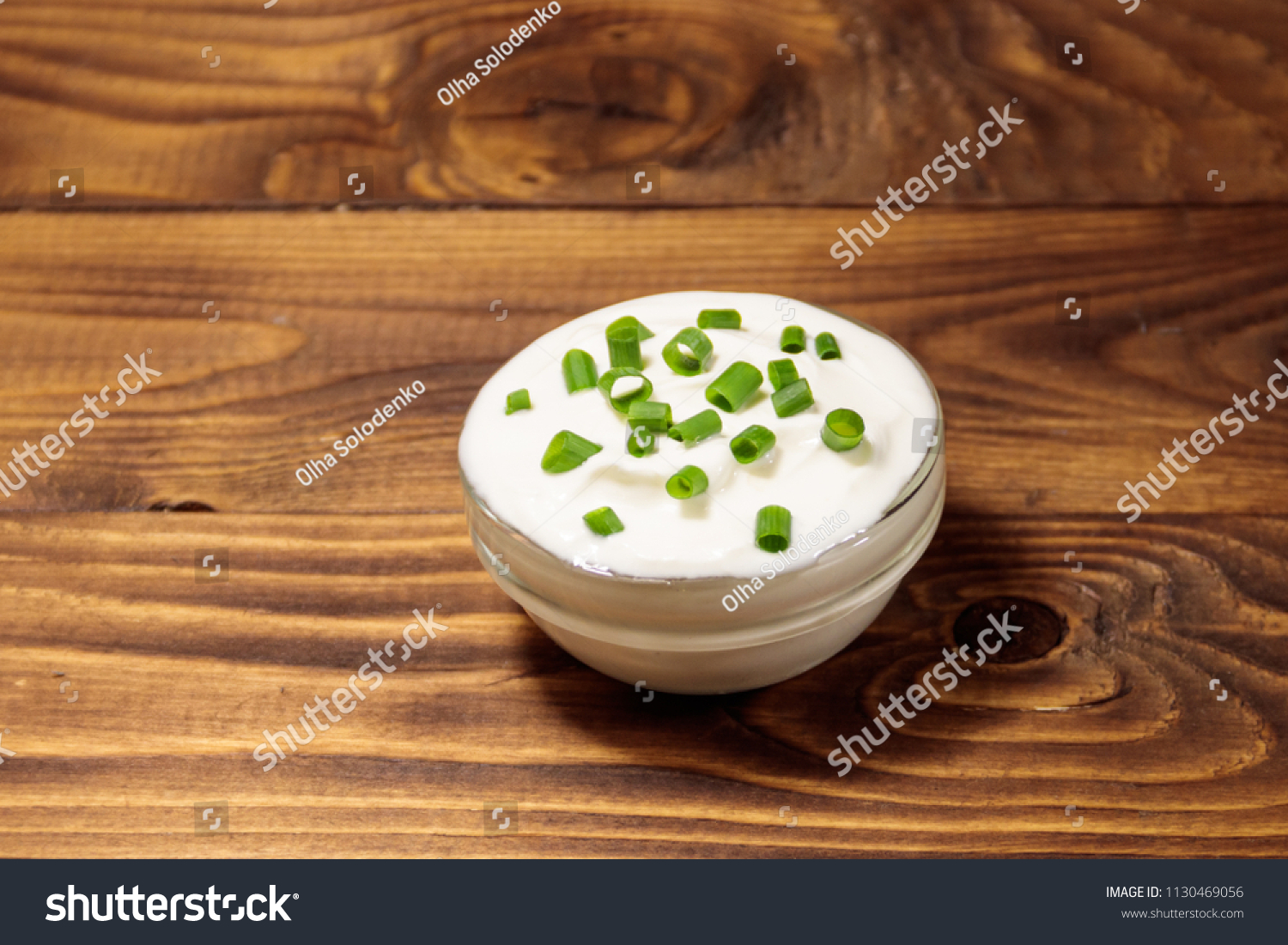 Sour cream with green onion in glass bowl on wooden table #1130469056