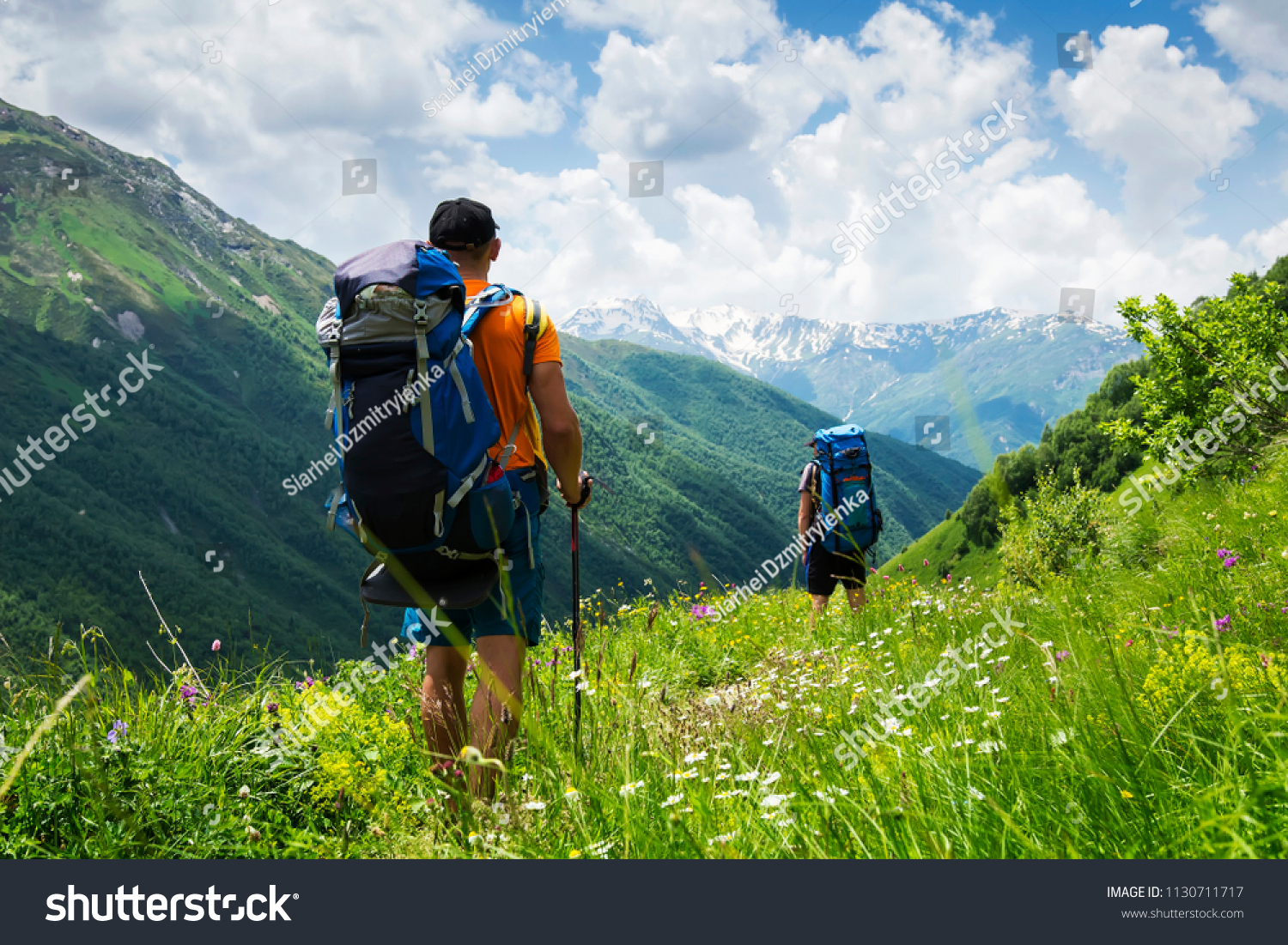 Tourists with hiking backpacks in mountain hike in Svaneti on summer day. Young guys go along the footpath through the mountains of Georgia. Tourists in beautiful mountain landscape. #1130711717