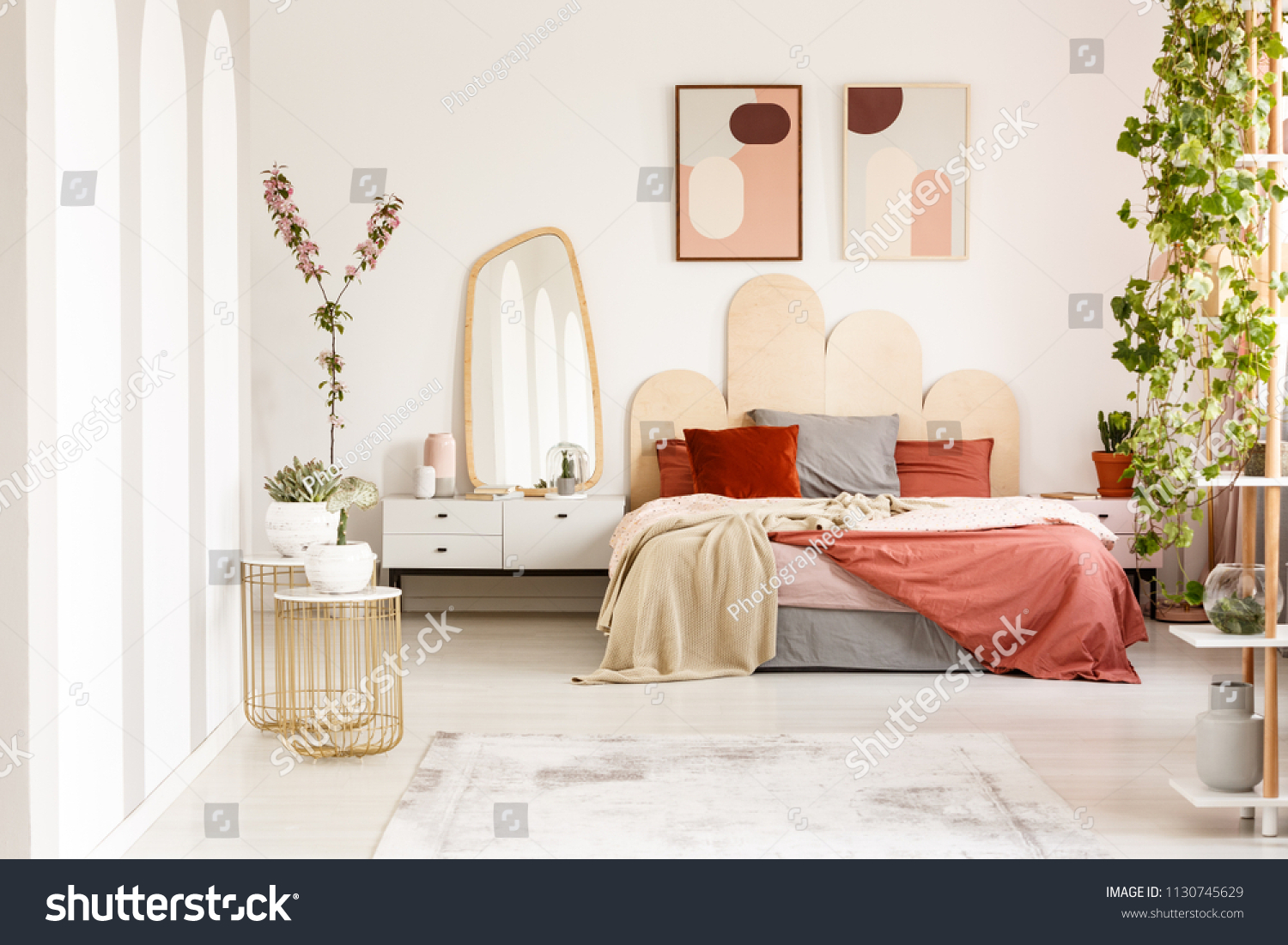 Blanket on bed with headboard under posters in modern bedroom interior with plants. Real photo #1130745629