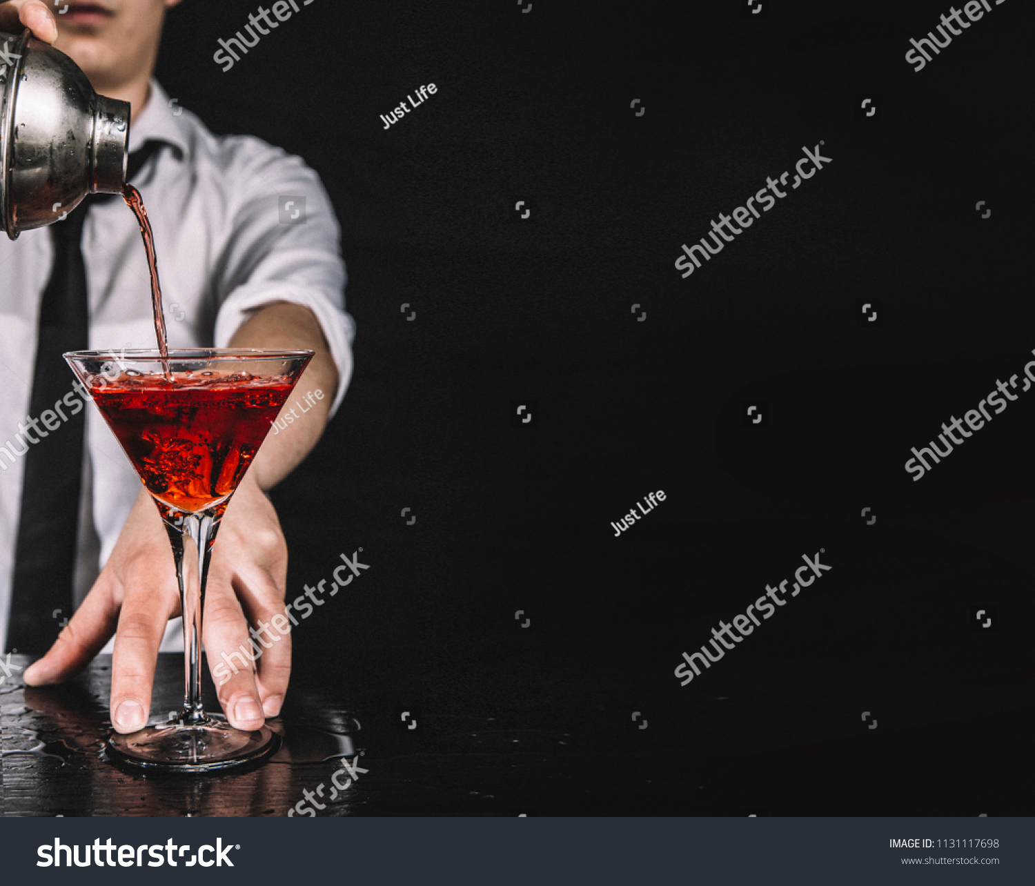 Expert barman making cocktail at nightclub.  Bartender preparing red cocktail at cocktail glass at the bar. Preparing of cosmopolitan cocktail. Red alcoholic drink in glasses on bar.  #1131117698