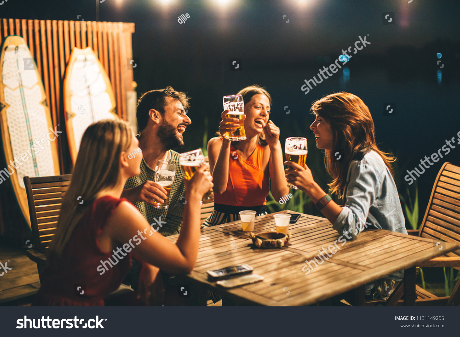 Group of friends drink beer on the terrace and toast during summer night #1131149255