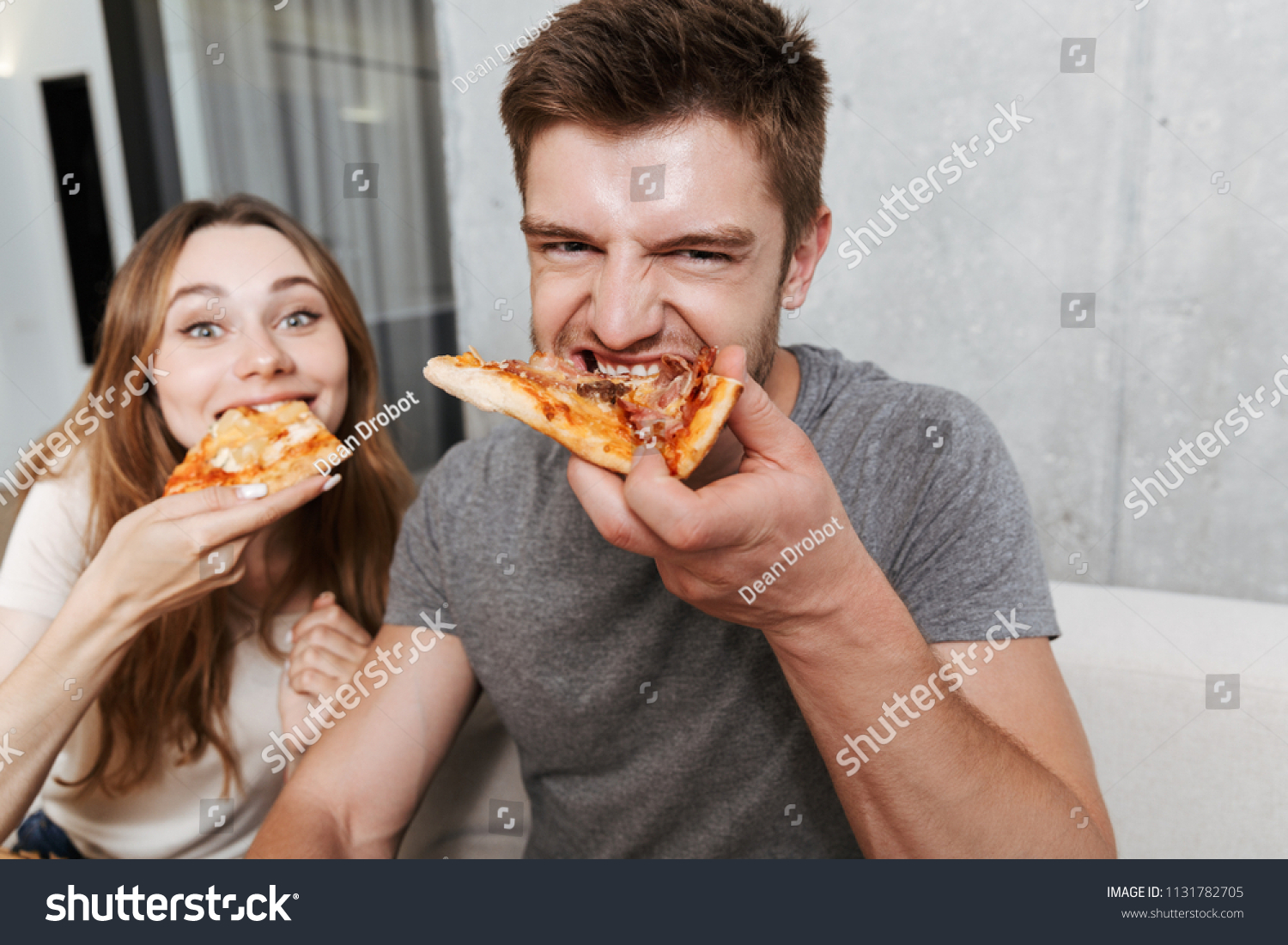 Close up of happy young couple eating pizza while sitting together on couch at home #1131782705