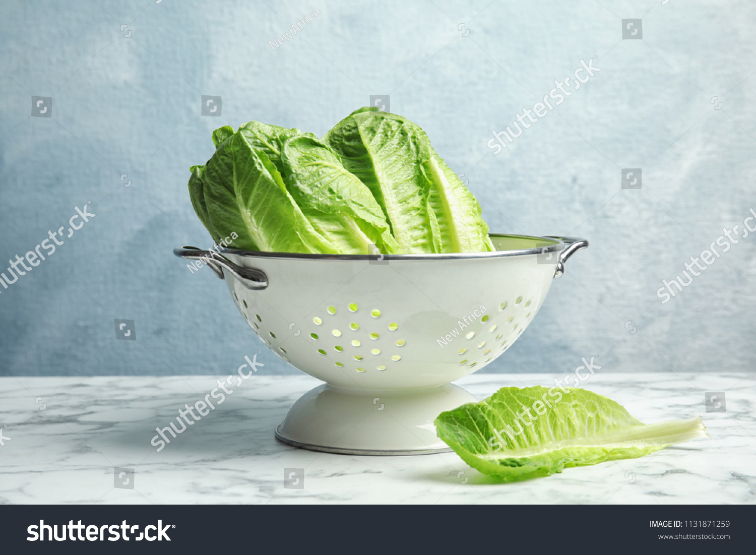 Colander with fresh ripe cos lettuce on marble table #1131871259