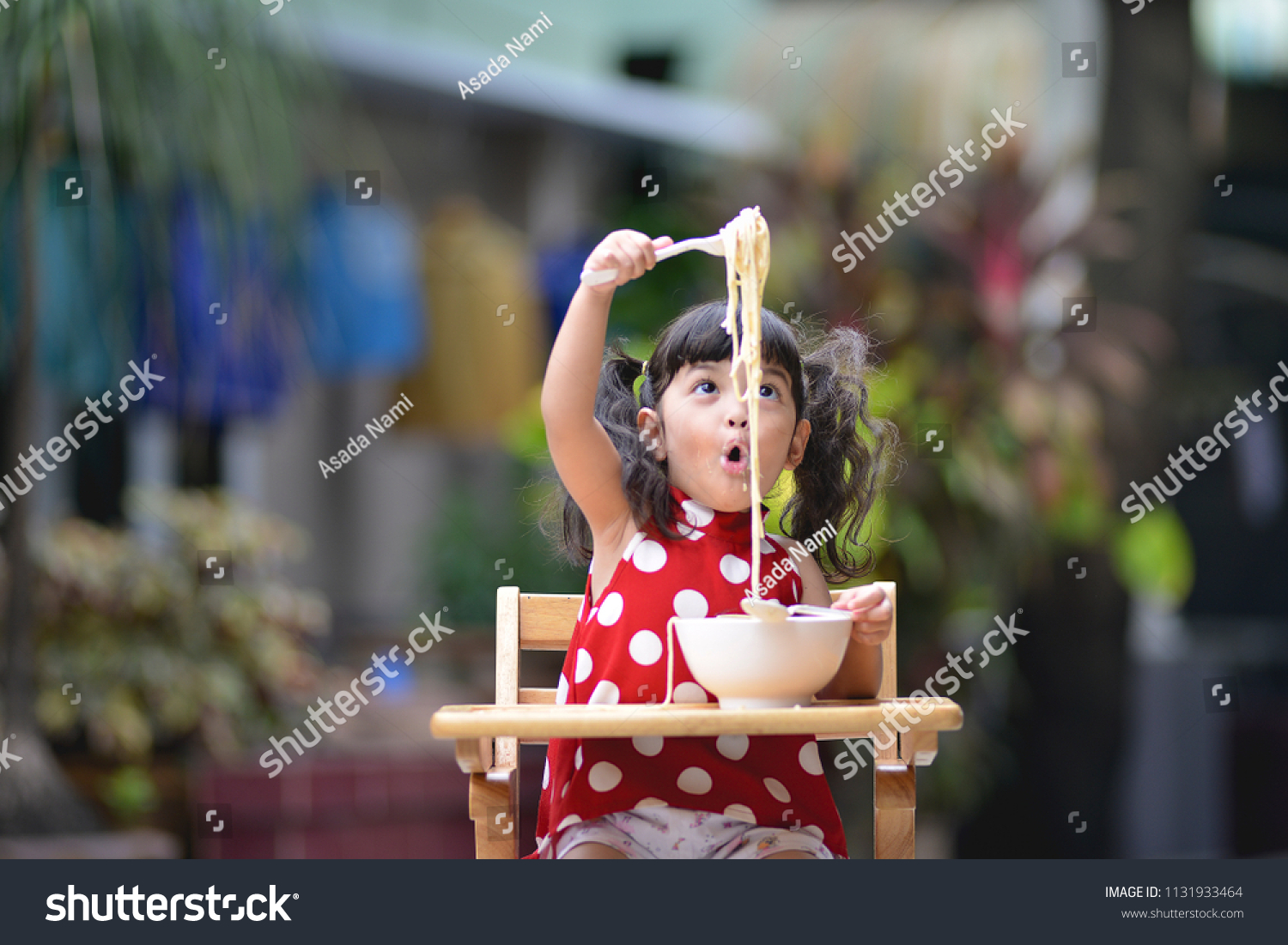 Asian little cute girl have fun while eating Italian spaghetti  white sauce or carbonara on the table in outdoor. kid have fun and joyful with eating #1131933464