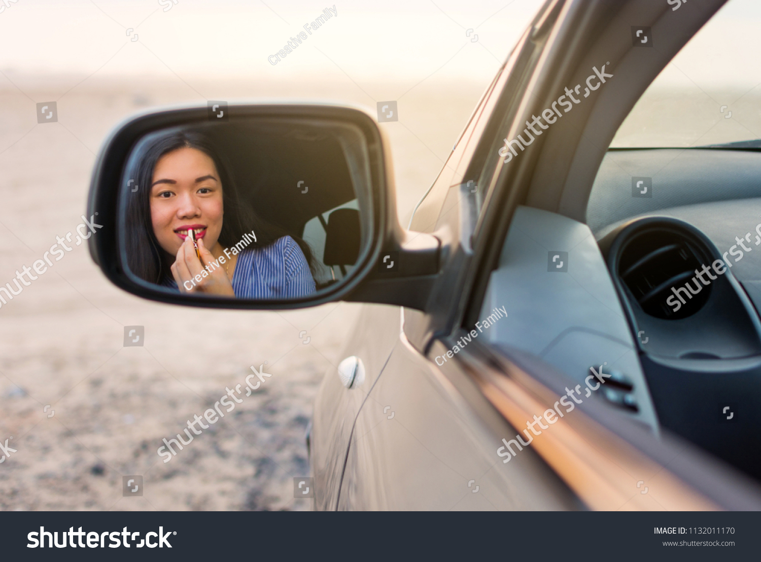 Female driver applying lipstick using rear mirror in a car #1132011170