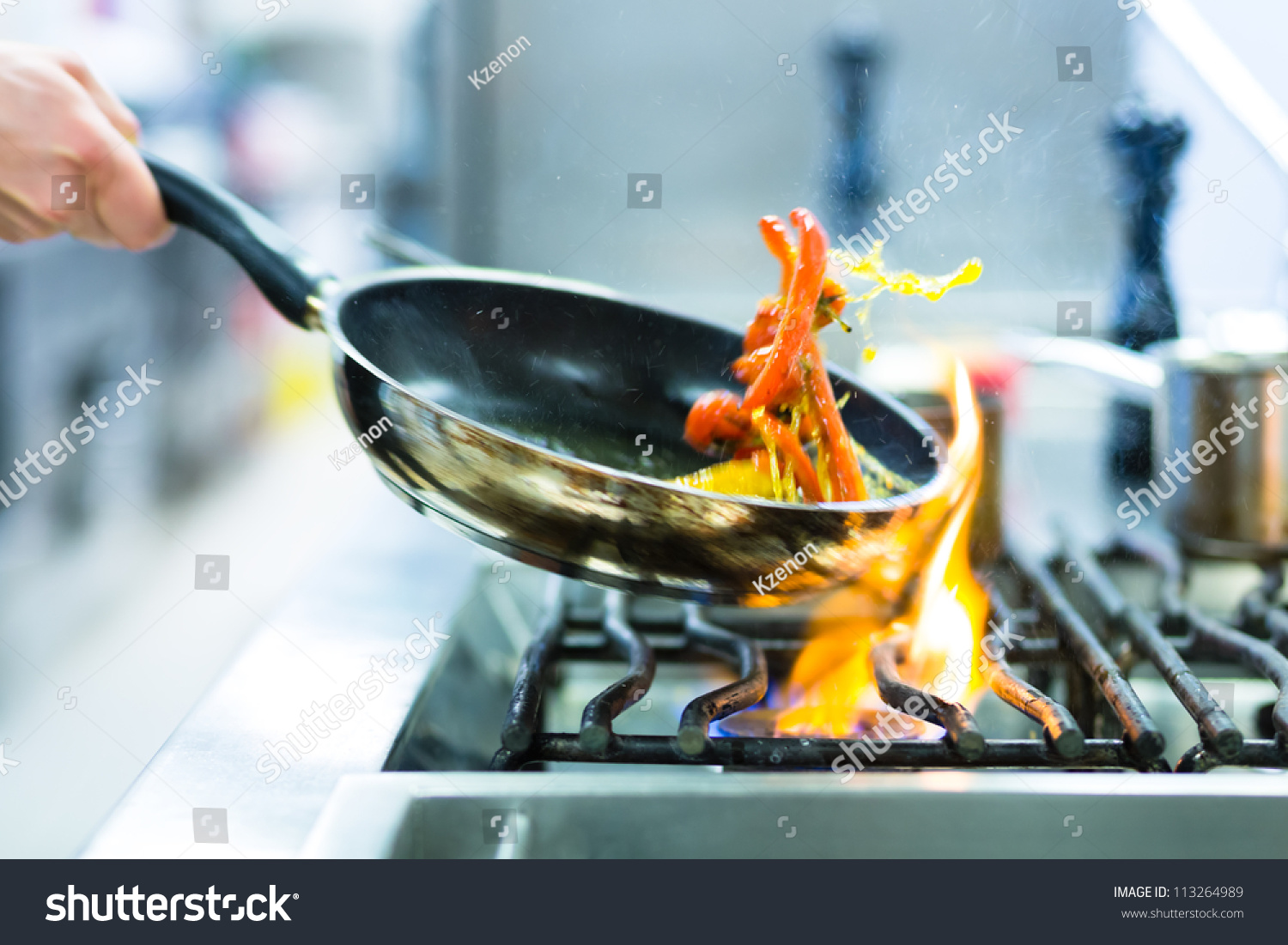 Chef in restaurant kitchen at stove with pan, doing flambe on food #113264989