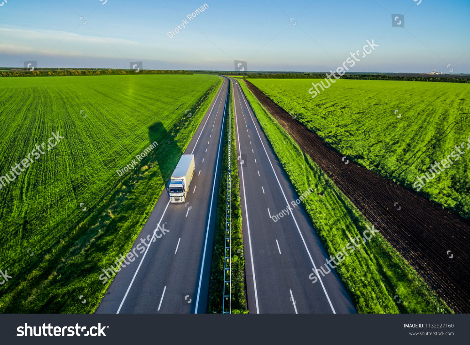 White trucks driving on asphalt road along the green fields in rural landscape. Road seen from the air. Aerial view landscape. shooting from a drone  #1132927160
