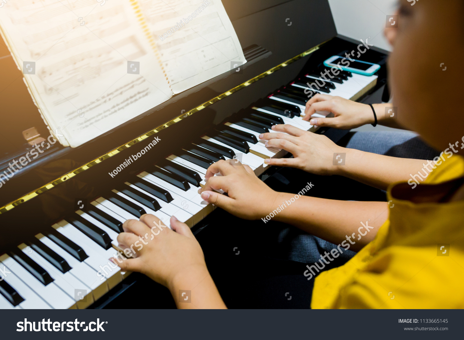  Blurry picture of woman teaching boy to play the piano with selective focus. Four hands from two people playing piano. with selective focus. #1133665145