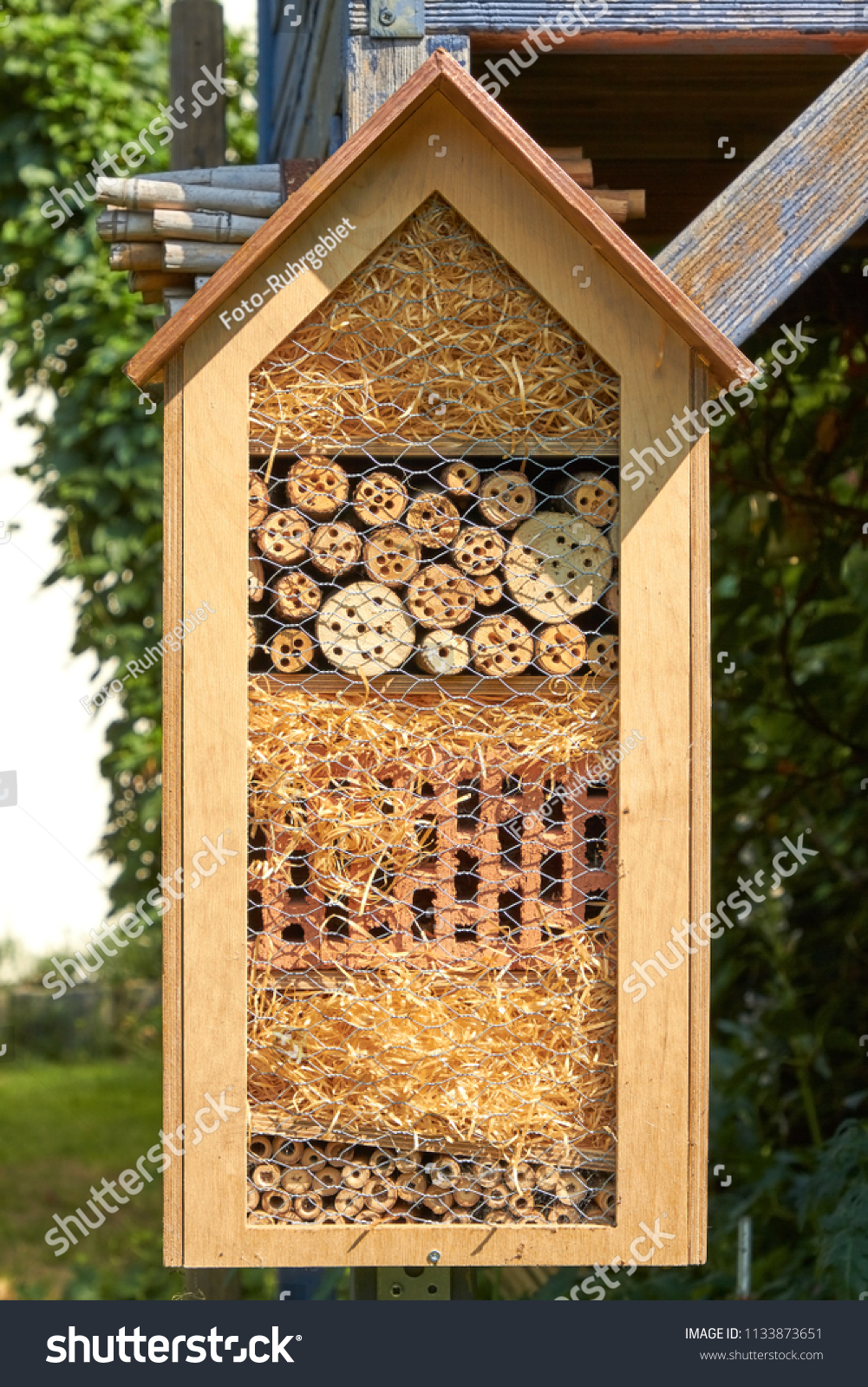 In a garden hangs an insect hotel in the sunlight. #1133873651