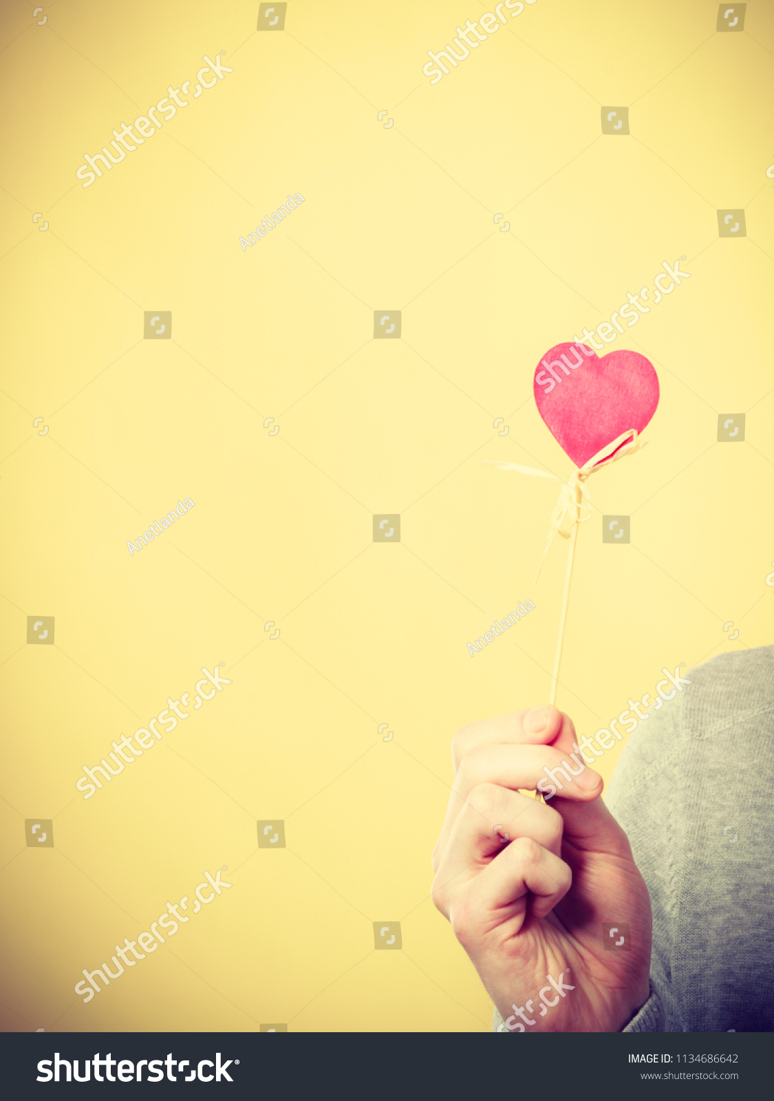 Symbolism romance relationship affection valentines concept. Male person holding heart on stick. Someone presenting love symbol on pole. #1134686642