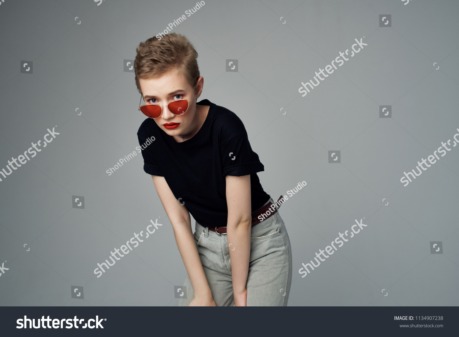  woman in a black T-shirt wearing glasses on a gray background                               #1134907238