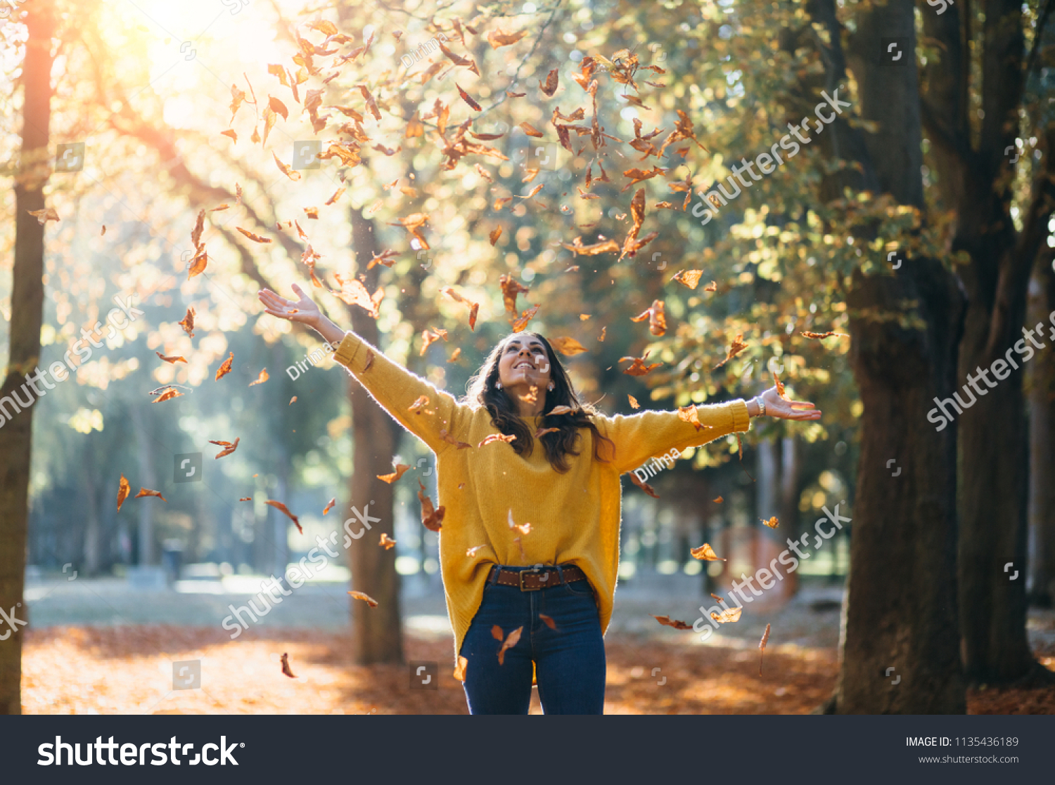 Casual joyful woman having fun throwing leaves in autumn at city park. #1135436189