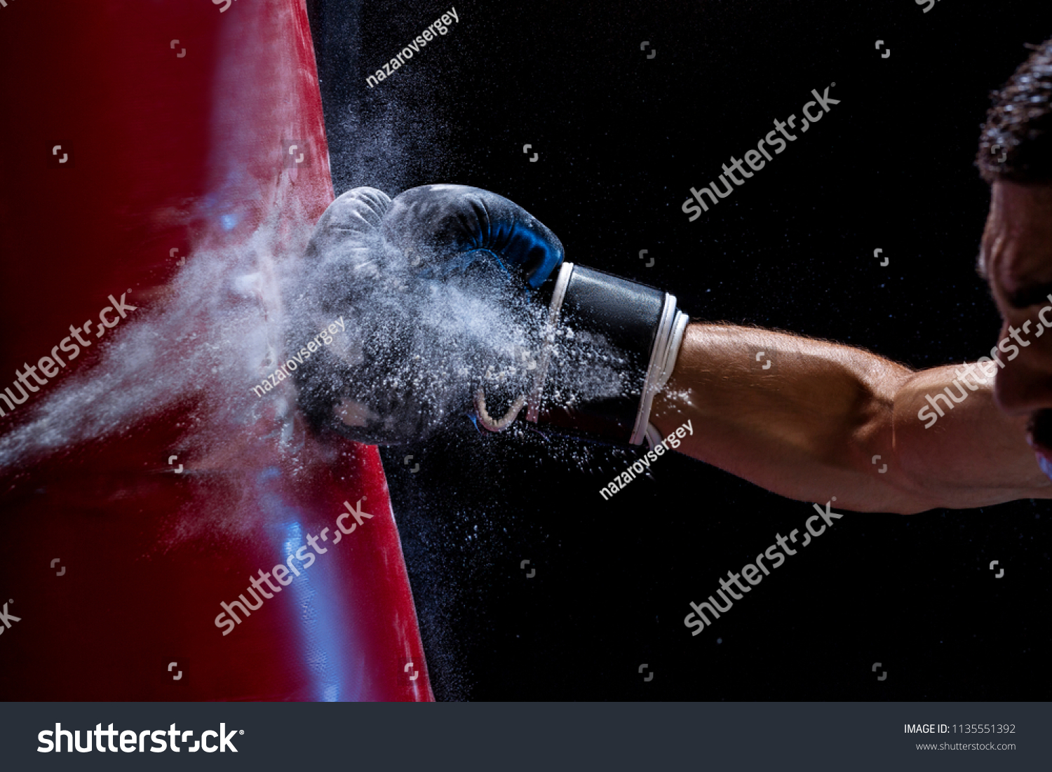 Close-up hand of boxer at the moment of impact on punching bag over black background #1135551392