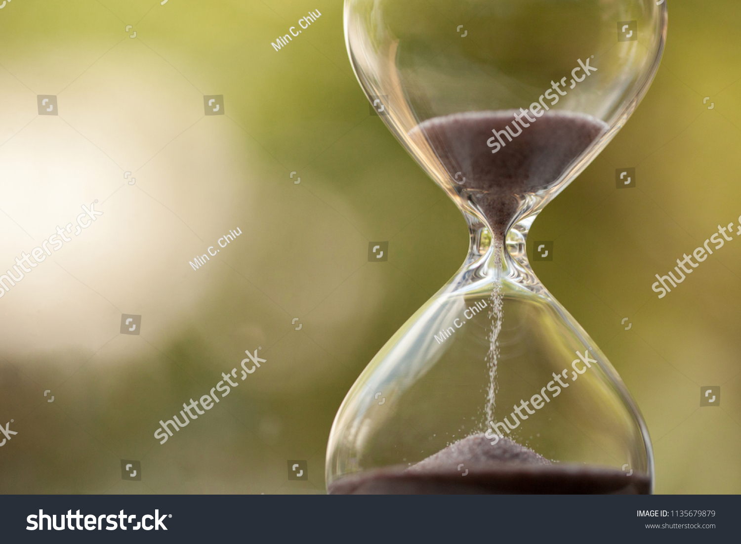 Modern Hourglass with green background -- sand trickling through the bulbs of a crystal sand glass. every second counts. symbol of time. countdown. #1135679879