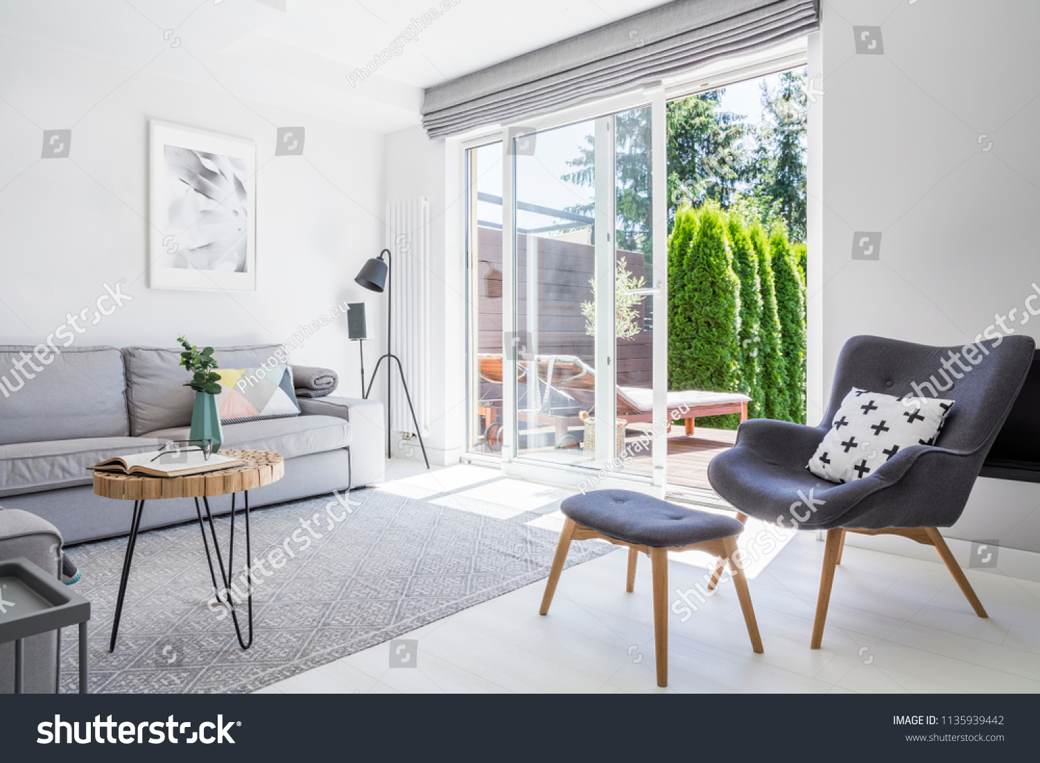 Armchair with patterned pillow and stool in living room interior with grey sofa and posters. Real photo #1135939442