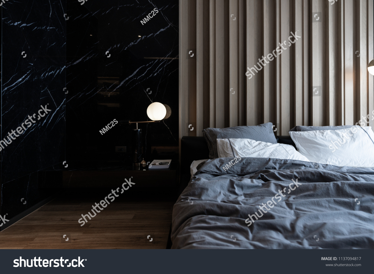 Cozy bedroom corner with nice black marble table lamp in mid century style in front of  wooden strip composition  headboard and natural black marble on the wall #1137094817