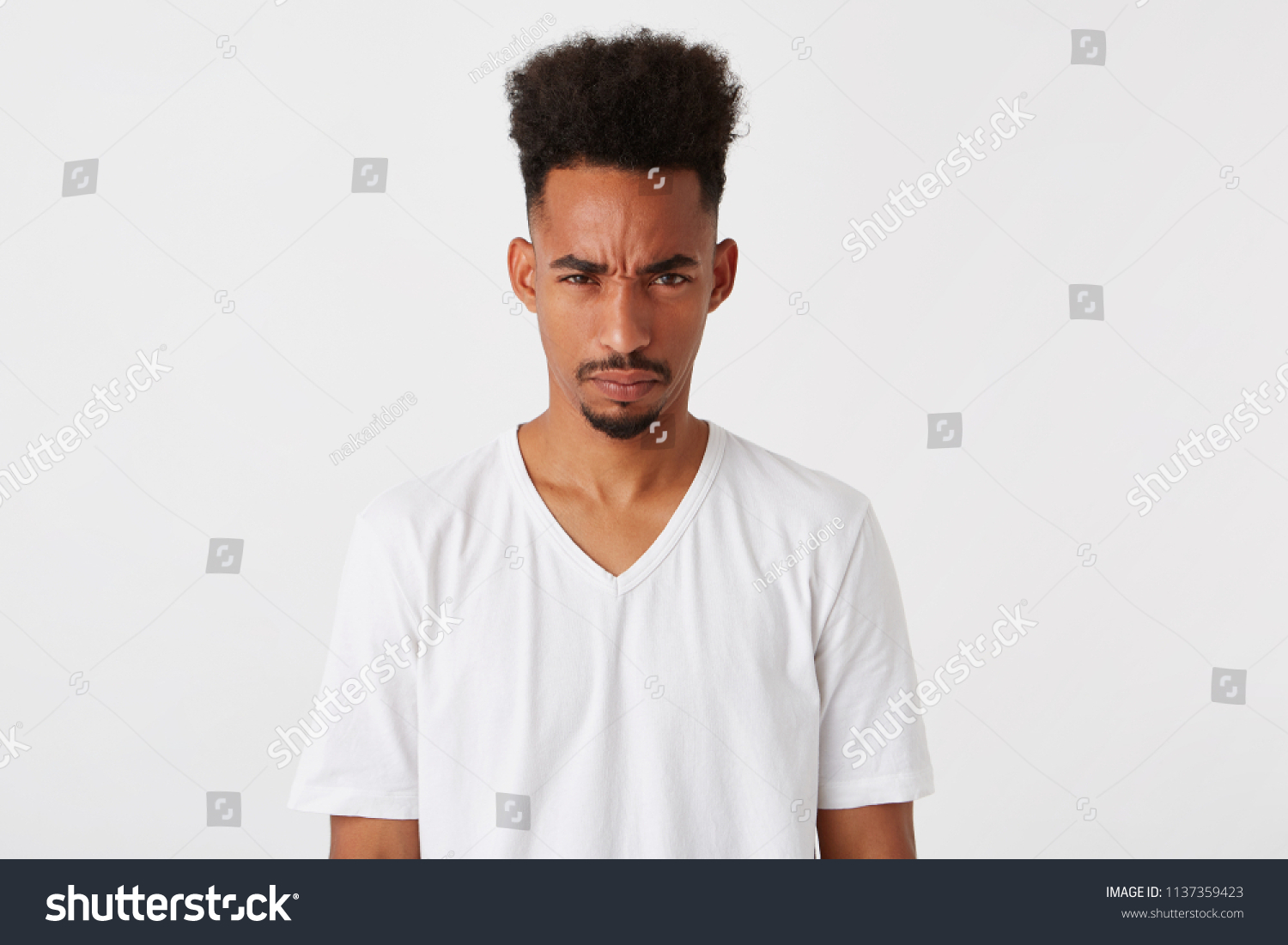 Portrait of mad displesed african american young man with afro hairstyle wears t shirt feels angry and irritated isolated over white background Looks directly in camera #1137359423
