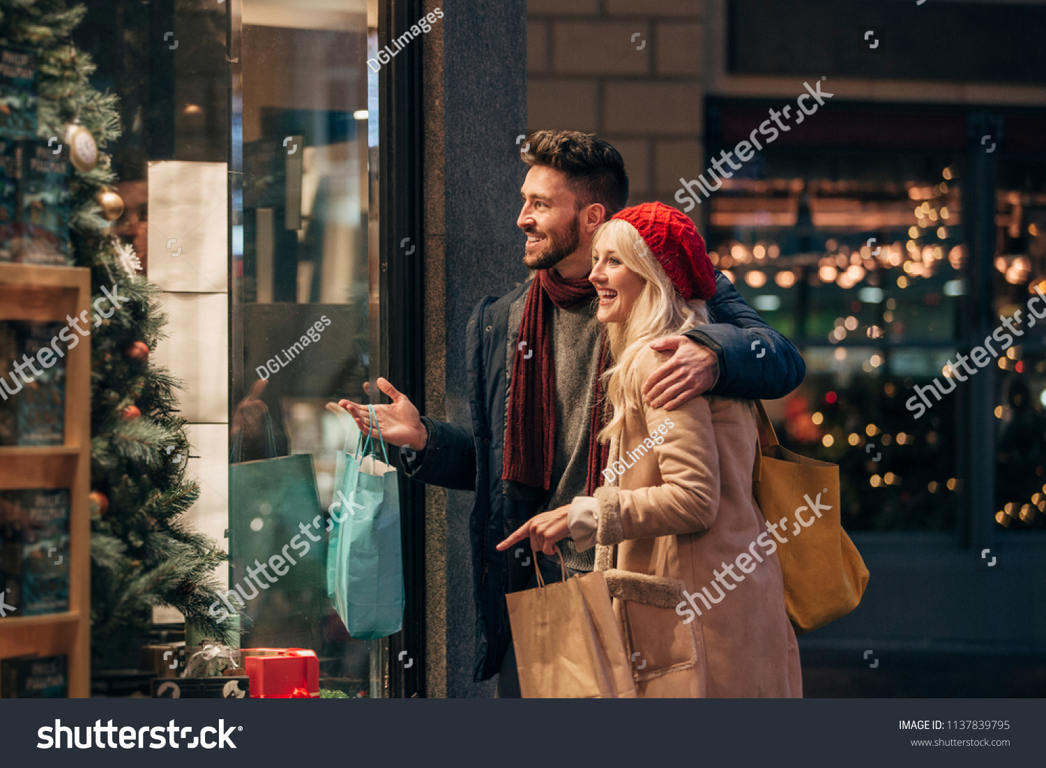 Side view of a couple doing some window shopping at christmas. The mid adult male has his arm around the mid adult female and they are talking about wats in the window. #1137839795