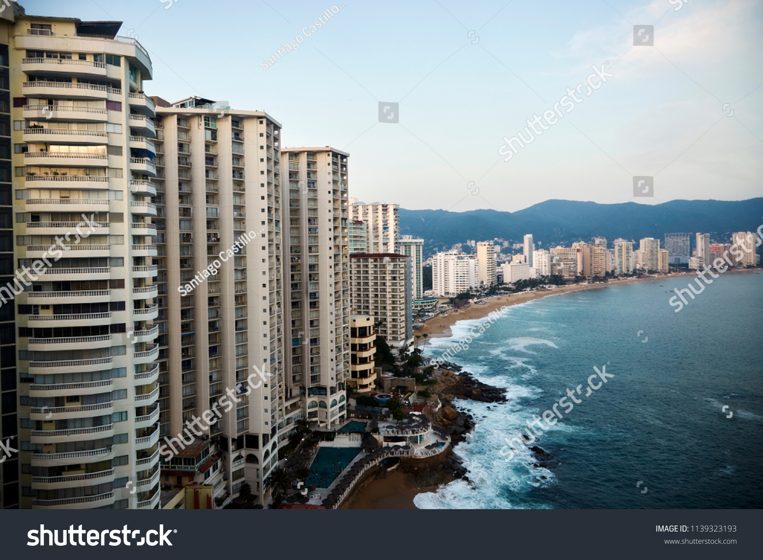 Acapulco bay with its characteristic line of hotels in front of a tiny beach line with a beautiful blue ocean on a sunny summer day #1139323193