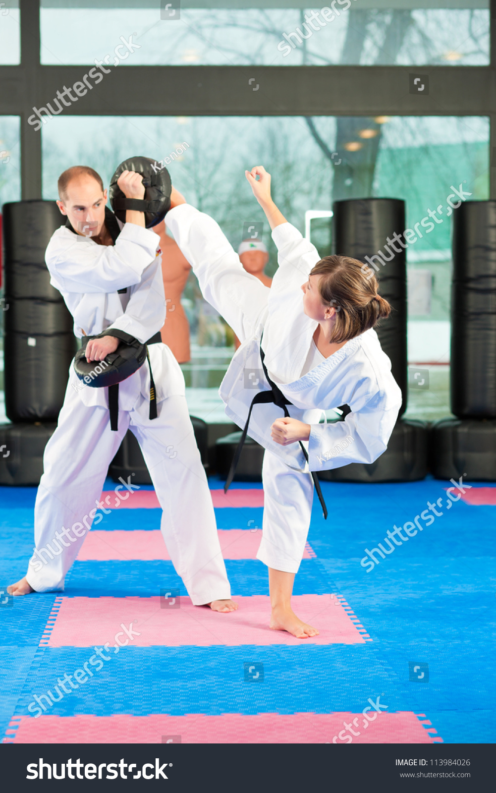 People in a gym in martial arts training exercising Taekwondo, both have a black belt #113984026