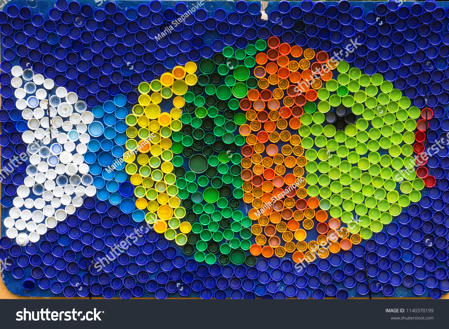 Fish mosaic decoration made of colorful plastic bottle caps . Summer season and travel concept. Handmade crafts. Recycling art. #1140370199