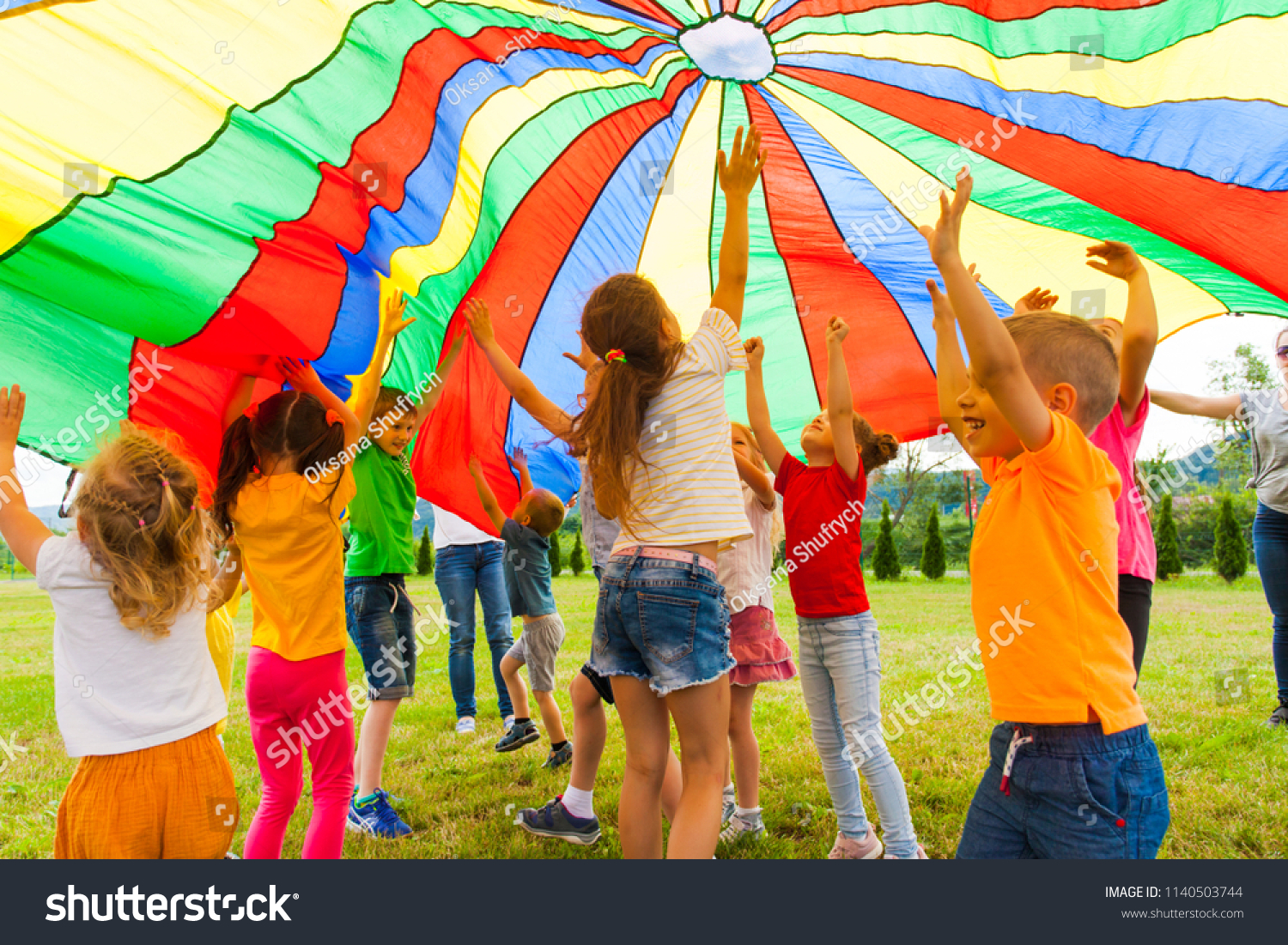 Joyous classmates jumping under colorful parachute #1140503744