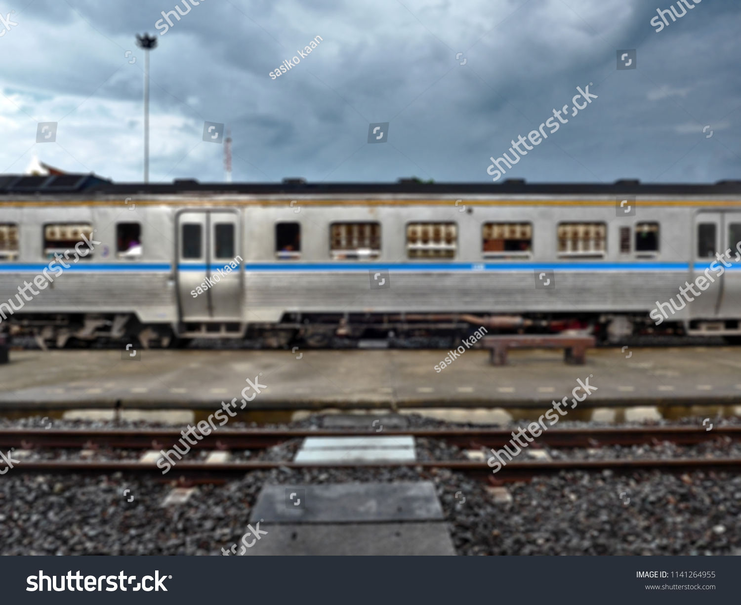 Blurry image and out of focus with dry brush filter : The old blue and silver wagon with windows of train parked at a station platform in  Thailand  #1141264955