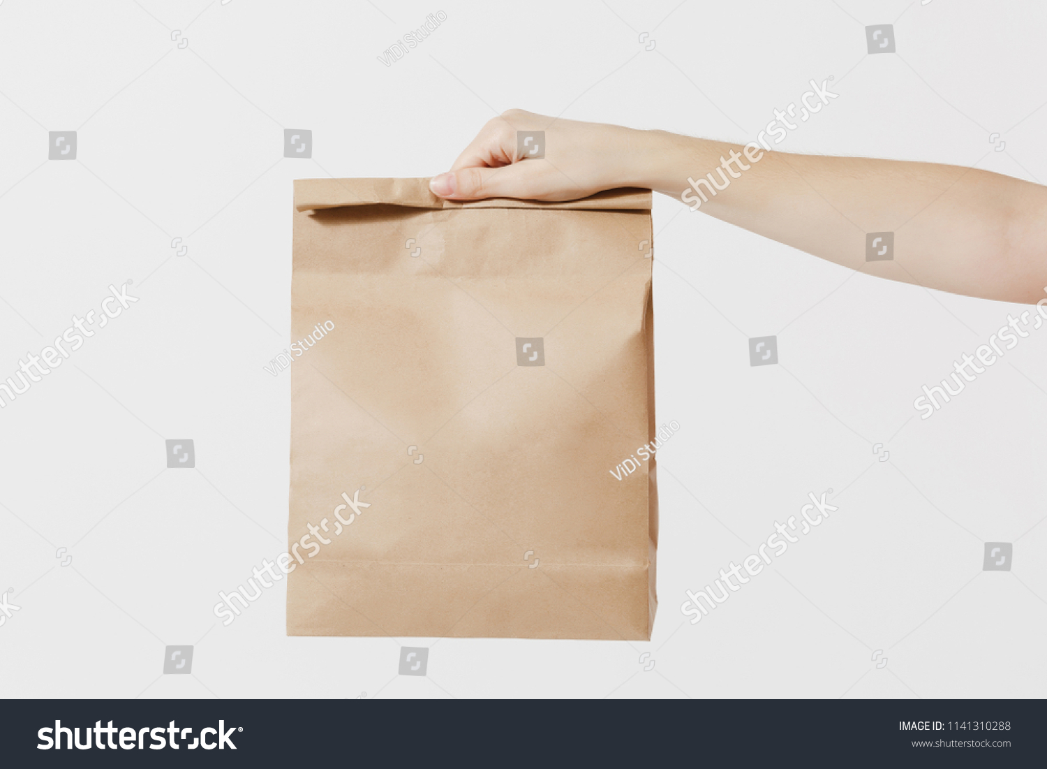 Close up female holds in hand brown clear empty blank craft paper bag for takeaway isolated on white background. Packaging template mock up. Delivery service concept. Copy space. Advertising area #1141310288