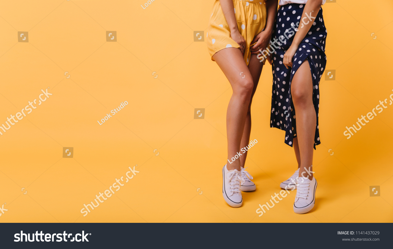 Shapely girls in white gumshoes standing on bright yellow background. Photo of female legs with tanned skin. #1141437029
