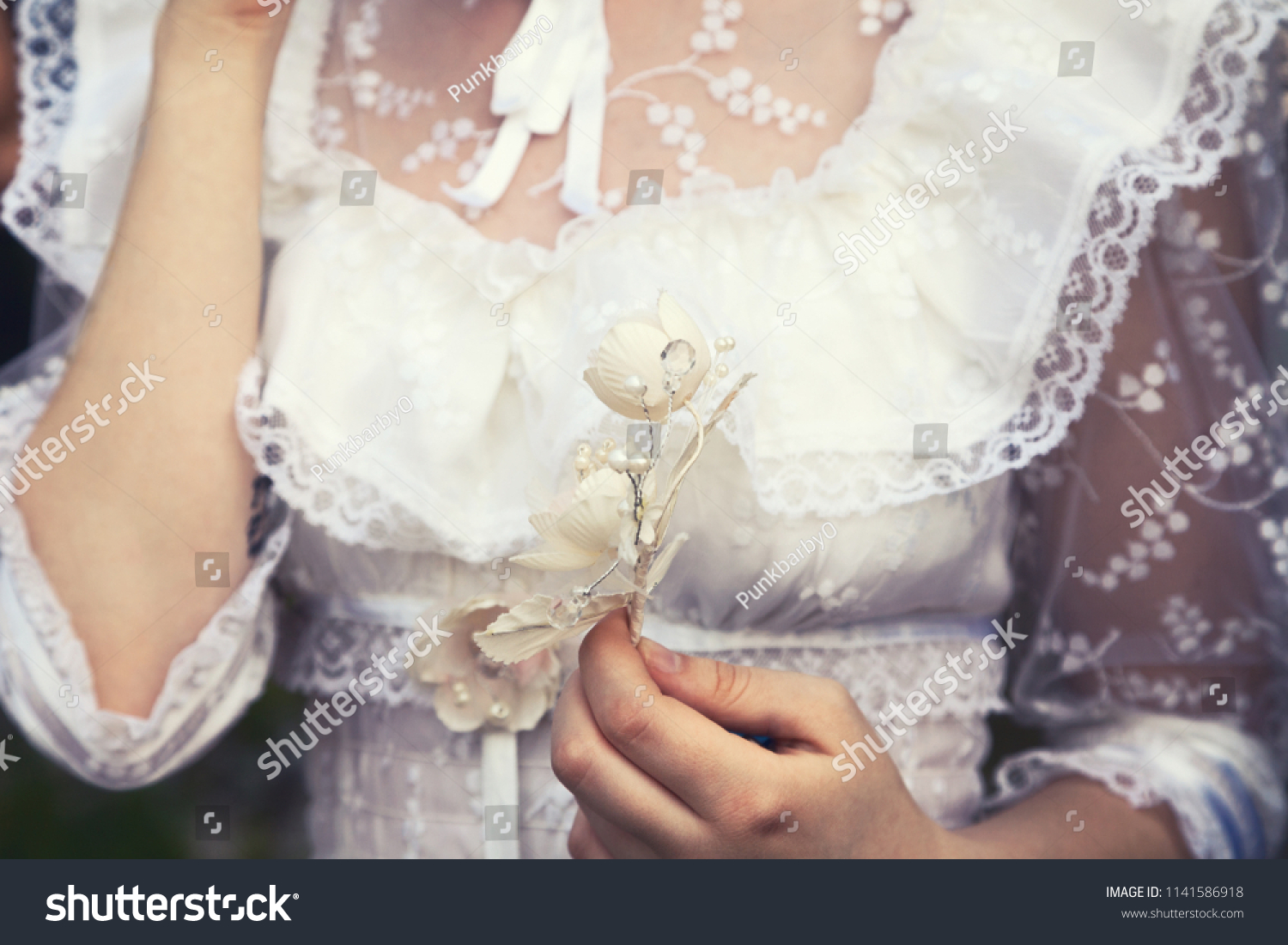 Young virgin girl in a white lace wedding dress holding a flower. Tender delicate woman at a wedding  #1141586918