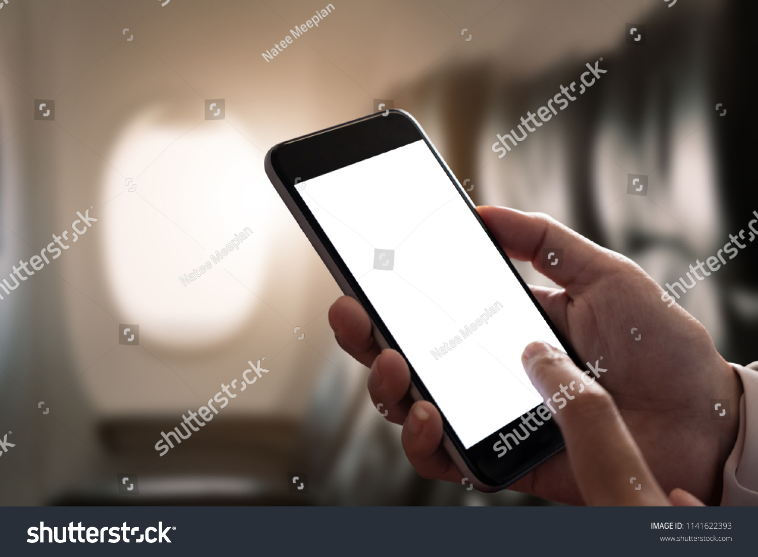 Mockup image of a hand holding a smart phone with blank desktop screen on airplane window, Blank screen mobile phone for graphic display montage #1141622393