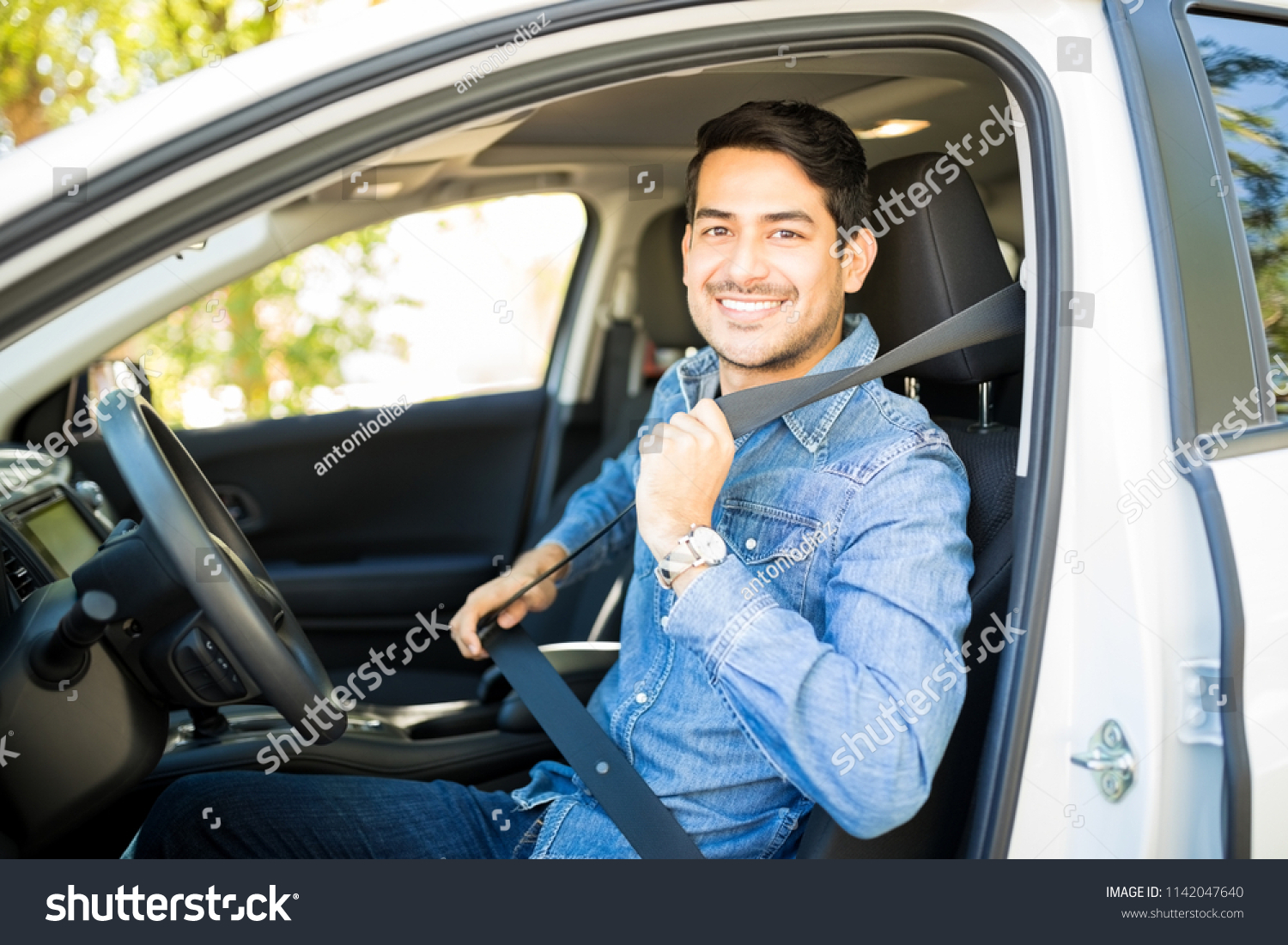 Portrait of handsome young man sitting in driving seat of car and wearing seatbelt for safety #1142047640