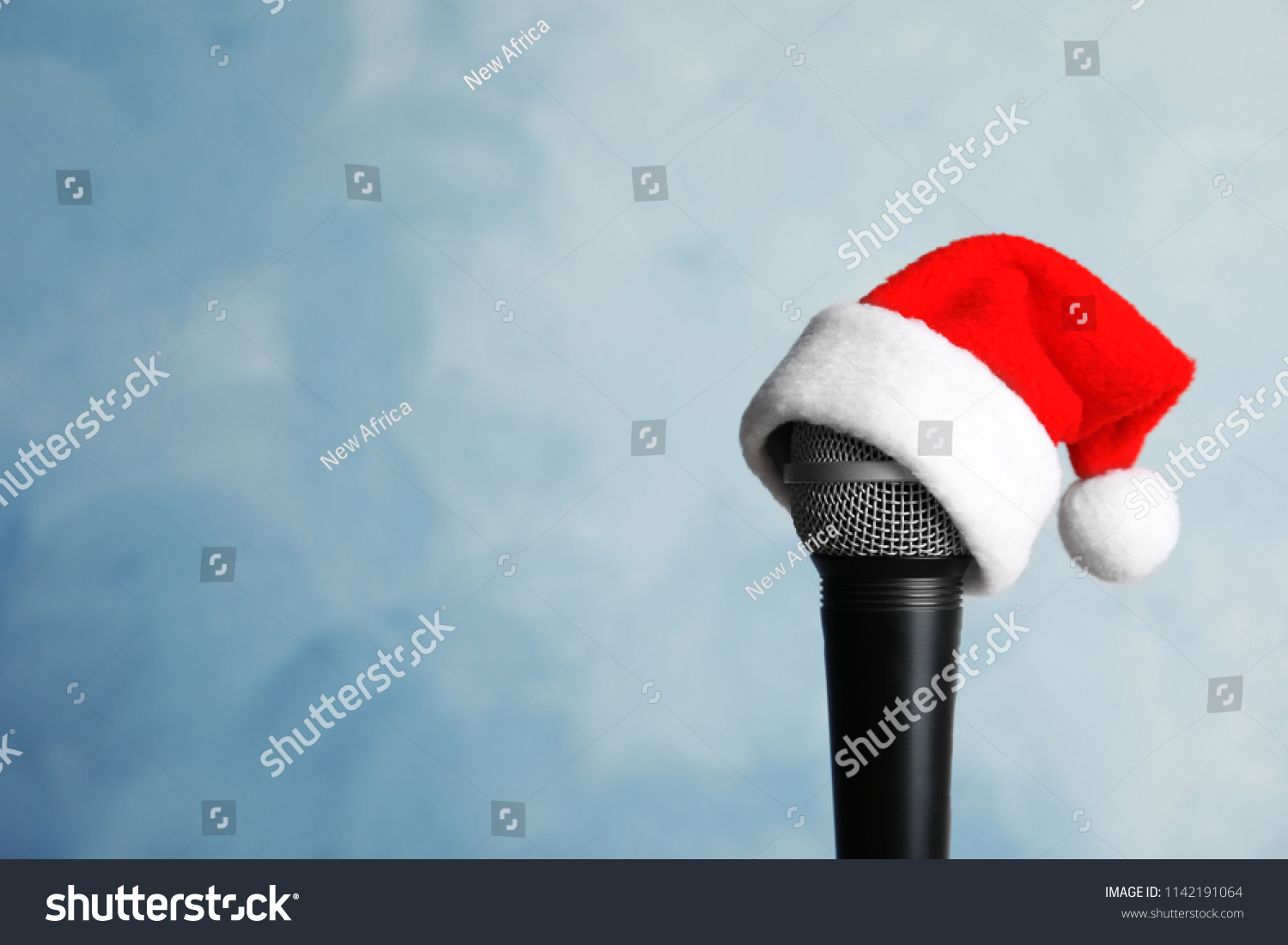 Microphone with Santa hat on color background. Christmas music concept #1142191064