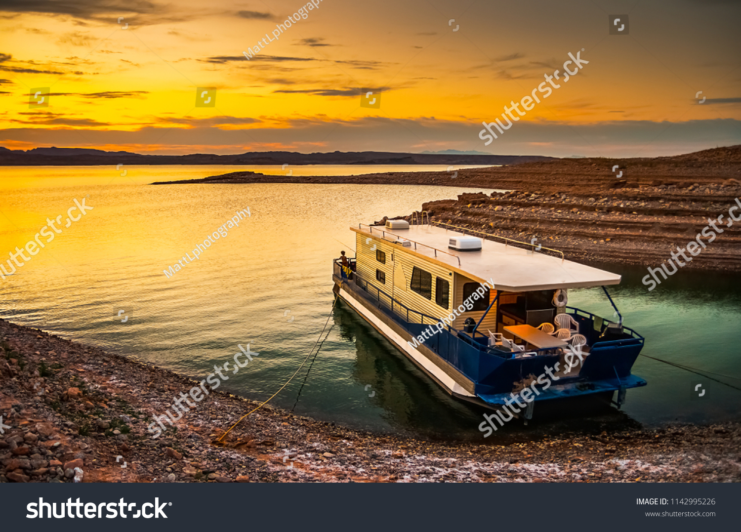 Beautiful and scenic landscape of the Lake Mead National Recreation Area with a houseboat moored to the shores of a bay with a dramatic sky at sunset, Nevada. Vacation and tourism concept. #1142995226