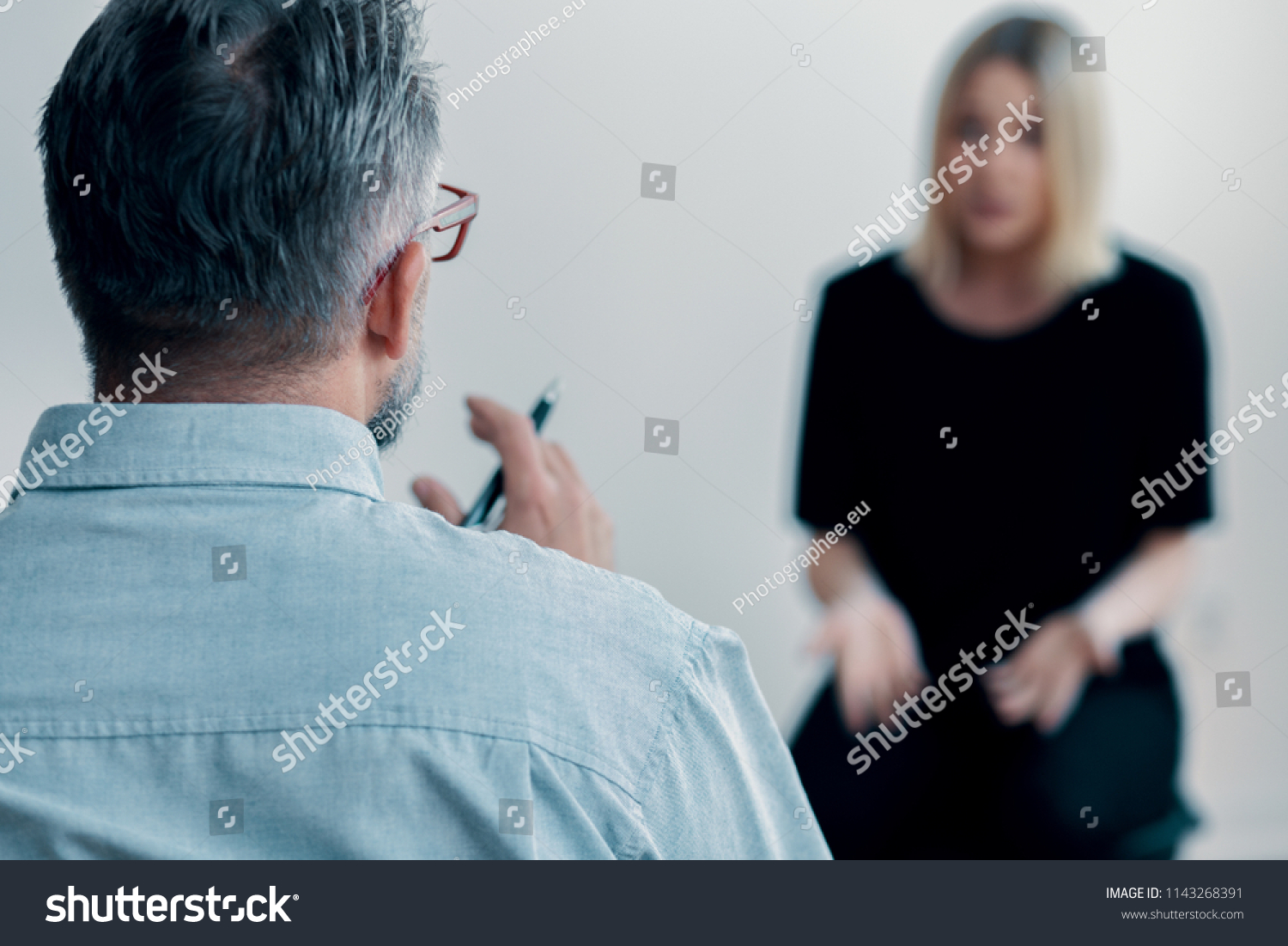 Close-up of a therapist holding a pen talking to his blurred female patient #1143268391