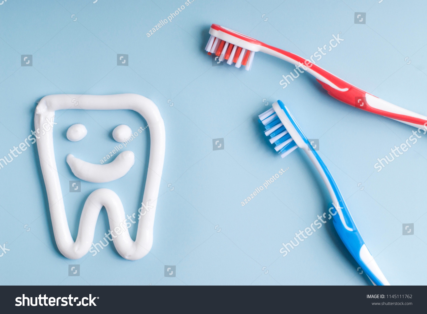 Toothpaste in a form of a smiling tooth. Red and blue toothbrushes. Toothpaste on blue. Dental hygiene. #1145111762