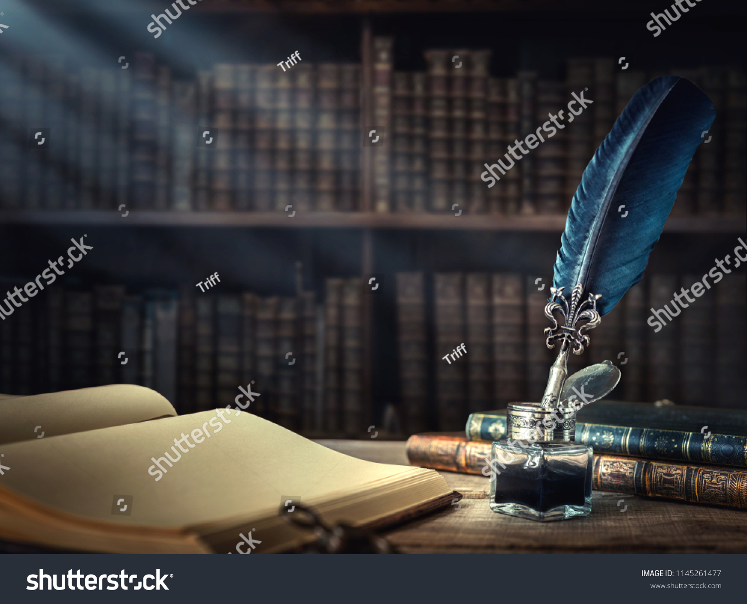 Old quill pen, books and vintage inkwell on wooden desk in the old office against the background of the bookcase and the rays of light. Conceptual background on history, education, literature topics. #1145261477