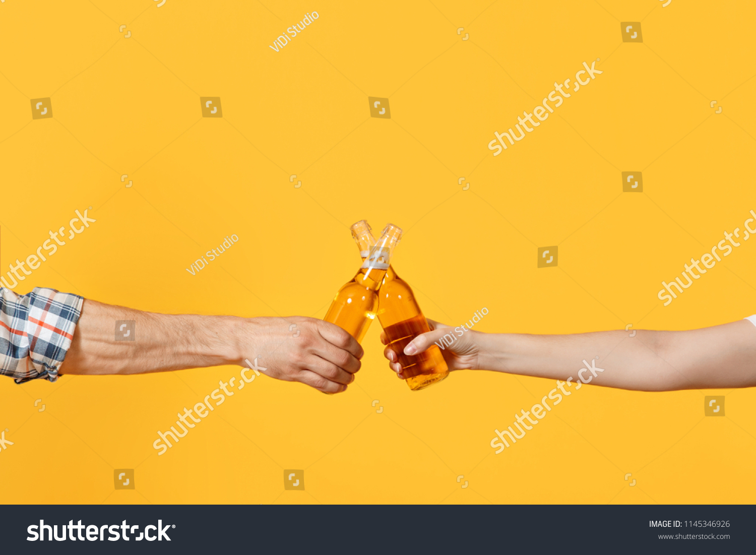 Close up cropped of woman and man two hands horizontal holding lager beer glass bottles and clinking isolated on yellow background. Sport fans cheer up. Friends leisure lifestyle concept. Copy space #1145346926