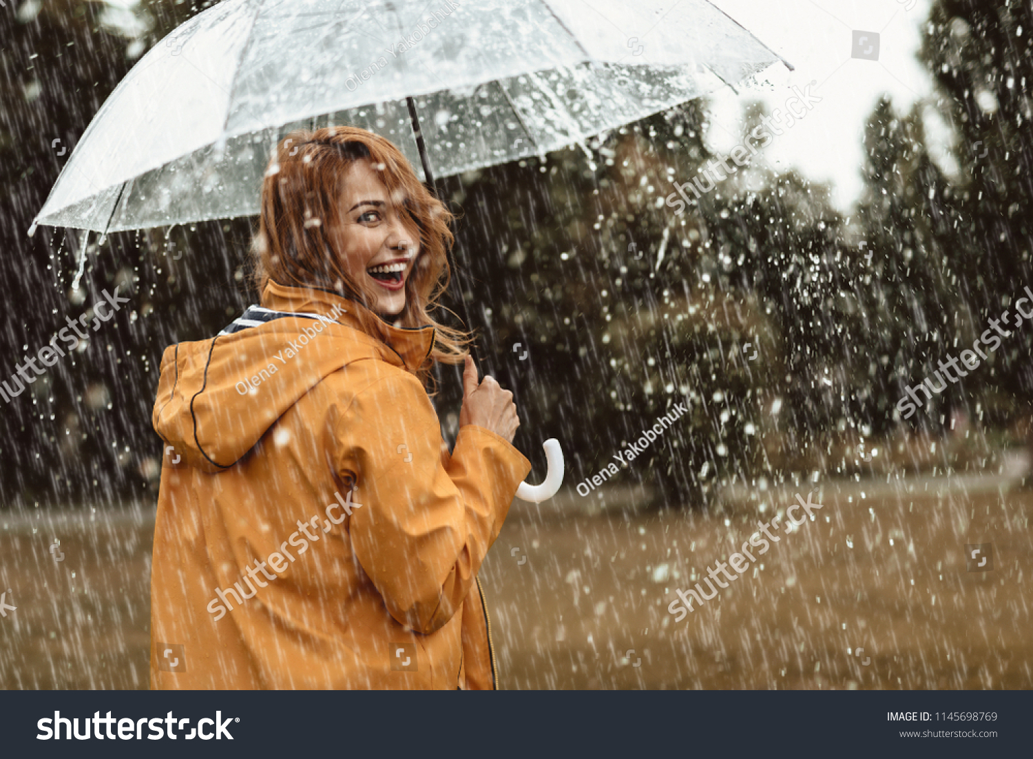 Cheerful pretty girl holding umbrella while strolling outside. She is turning back and looking at camera with true delight and sincere smile. Copy space in right side #1145698769