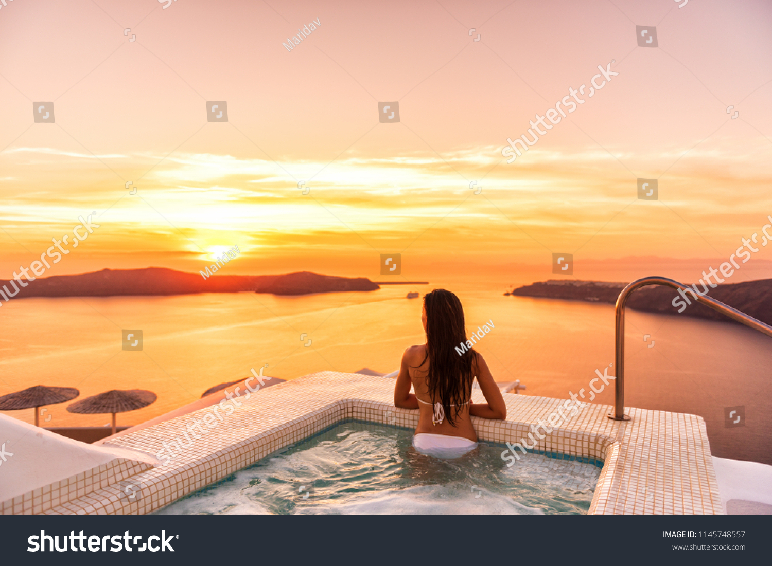 Luxury travel Santorini vacation woman swimming in hotel jacuzzi pool watching sunset. Europe resort destination holiday for honeymoon getaway. #1145748557