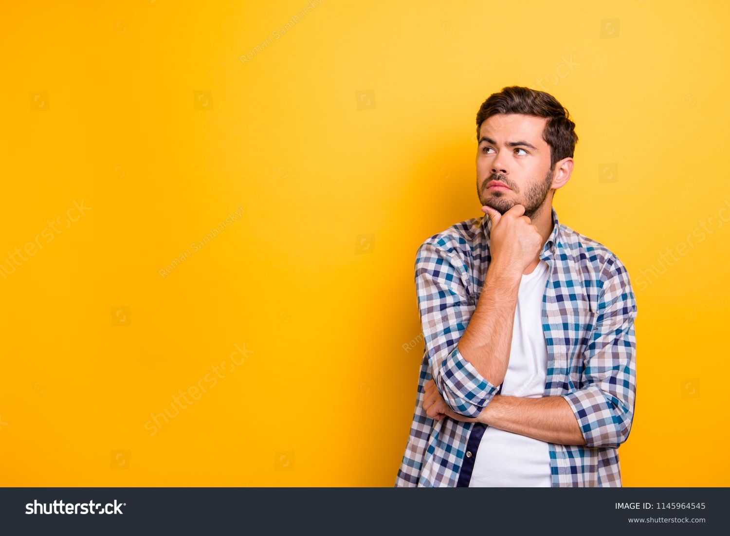 Close up portrait of thoughtful man who looks away touching his chin and weighs the pluses and minuses of the offer isolated on bright yellow background with copy space for text #1145964545