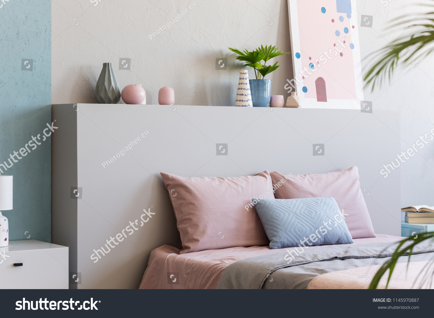 Poster on headboard of bed with pink pillows in bedroom interior with plants. Real photo #1145970887