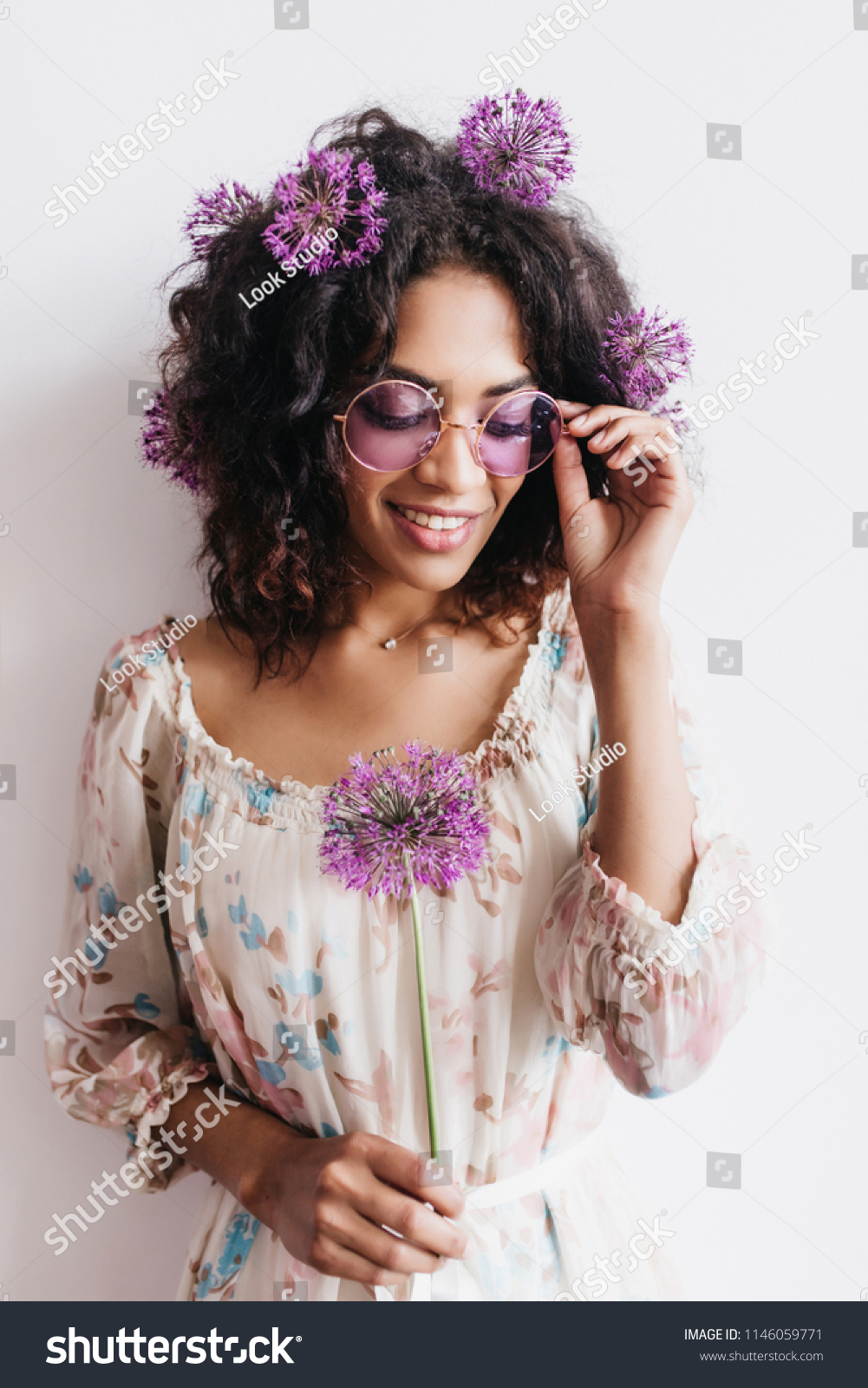 Adorable african girl with curly hairstyle holding allium. Studio shot of black lady in sunglasses posing with purple flowers. #1146059771