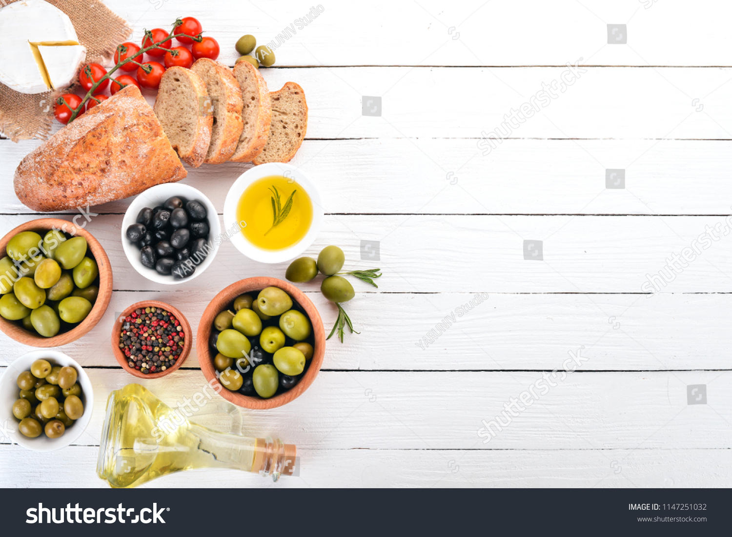Green olives and black olives, oil, bread, cheese and snacks. Italian cuisine. On a white wooden table. Top view. Free space for text. #1147251032