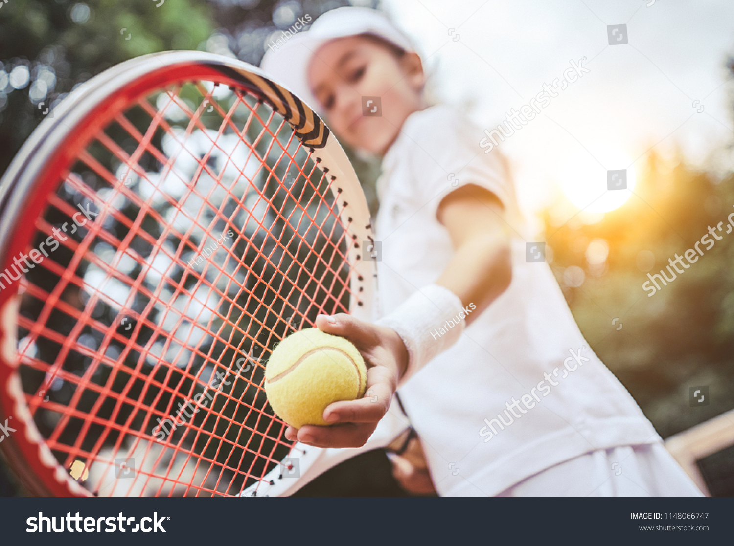 Sporty little girl preparing to serve tennis ball. Close up of beautiful yong girl holding tennis ball and racket. Child tennis player preparing to serve. #1148066747