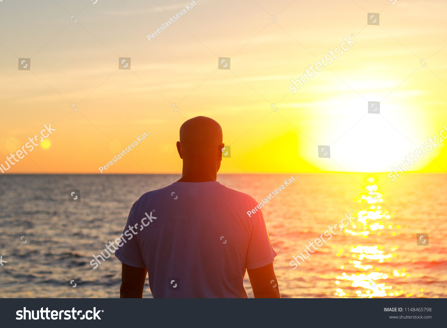 a man stands with his back looking at the sea and the sunset #1148465798