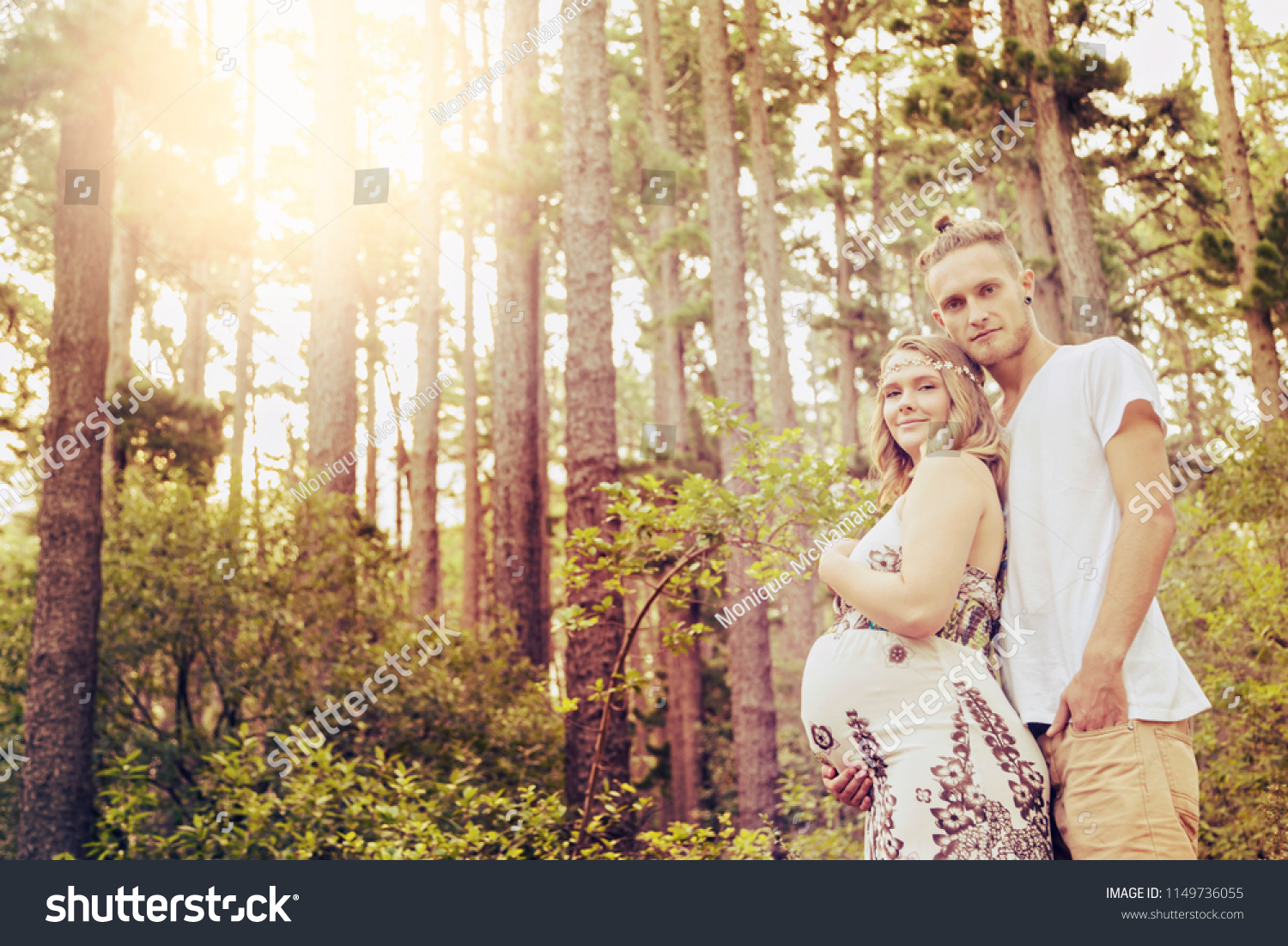 A young couple, - she very pregnant - walk through a sunny forest as she cradles her unborn child. #1149736055