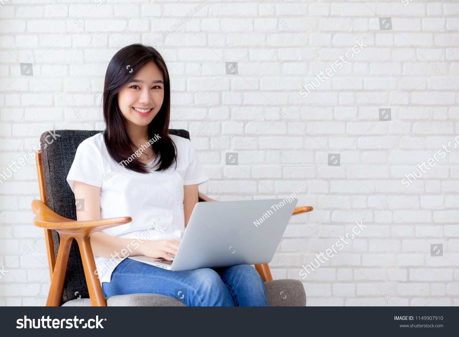 Beautiful of portrait asian young woman working online laptop sitting on chair on cement brick white background, girl using notebook computer, business concept. #1149907910