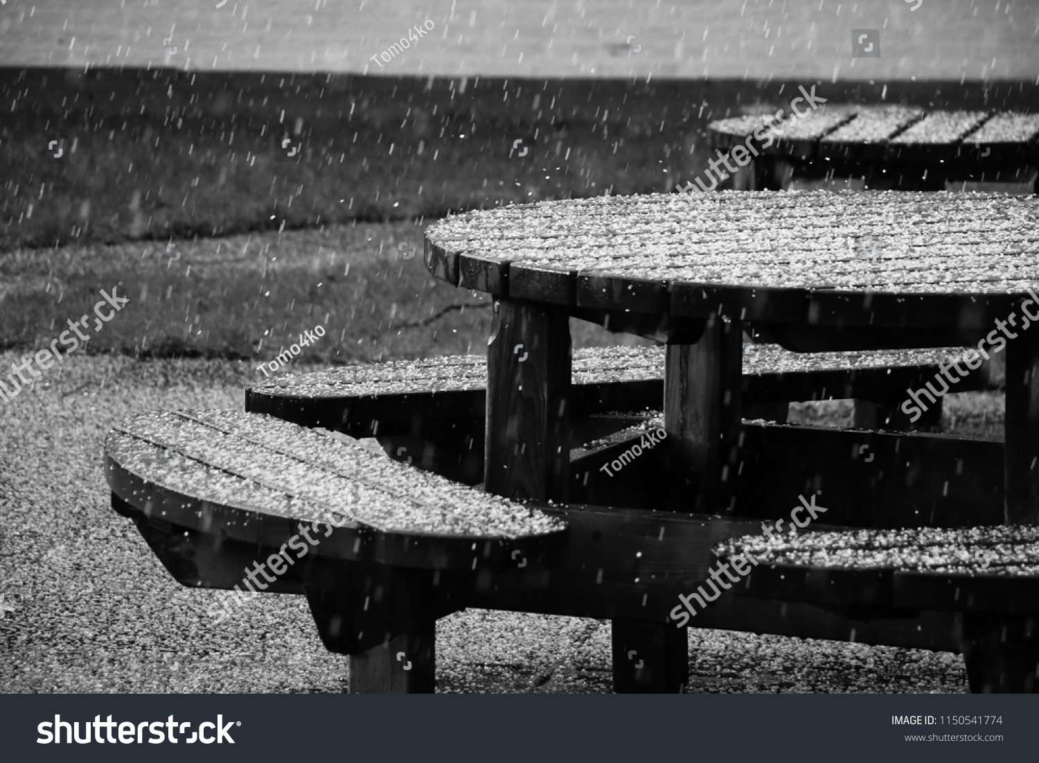 Wooden table with seats under a downpour. Sad and romantic, monochromatic picture.  #1150541774
